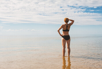 Sporty woman standing in the water of sea back pose and looking into the distance - 753883988