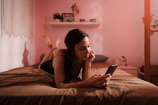 Happy woman using mobile phone lying on bed 