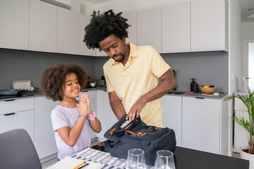 Father Helping Child To Prepare Her Backpack For School