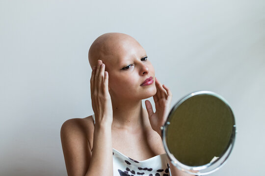 Confident young bald woman looking in mirror