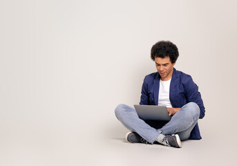 Focused young male entrepreneur doing online research over laptop while sitting on white background