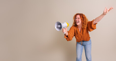 Cheerful young saleswoman with redhead and arm raised shouting over megaphone on white background