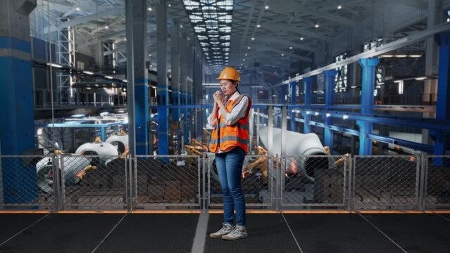Full Body Side View Of Asian Female Engineer With Safety Helmet Prays For Something While Standing In Factory Manufacture Of Wind Turbines