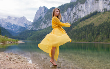 Young beautiful girl in a light yellow dress by the lake in the mountains