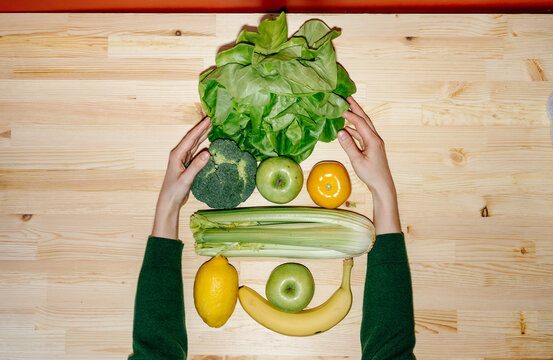 Green and yellow fruits and vegetables with hands on table 