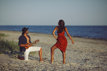 Happy couple in love sensual romance. Caucasian man playing ukulele serenading and girl in red...
