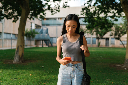 Young pensive Asian woman using smartphone in park