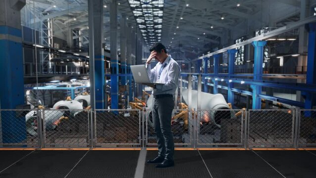 Full Body Side View Of An Asian Male Professional Worker Standing With His Laptop At The Center Of The Wind Turbine Factory, Typing And Dissapionted With Nodding His Head 
