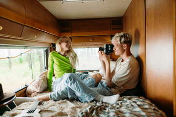 A man takes pictures of a woman sitting on a bed in a van