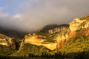 Fog shrouding the top of majestic gold-colored cliffs of golden gate highlands national park in the Drakensberg Mountains of South Africa, in the glow of the late afternoon sun