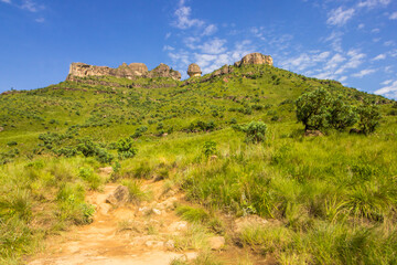 Fototapeta na wymiar Trail through the Grasslands of the Drakensberg mountains with bizarrely weathered sandstone formations and cliffs on the horizon.