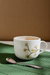 big ceramic hand painted mug and tea spoon on green mat with window light and hard shadows