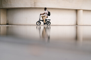 Male college student riding electric bike by building