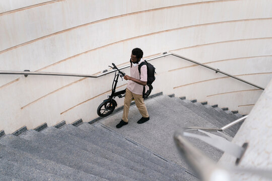 Male student carrying scooter walking upstairs in city