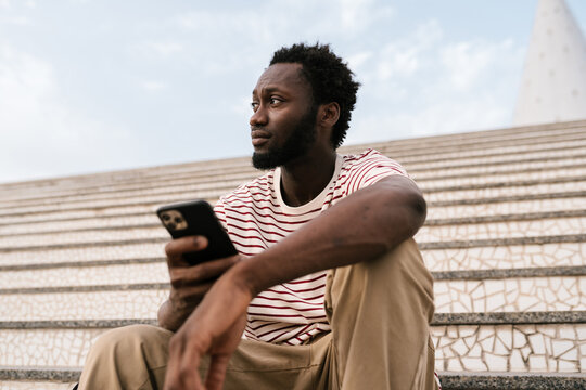 Black guy sitting on staircase with mobile phone