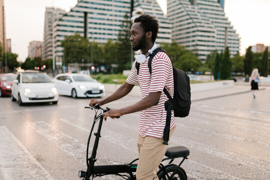 Cool black guy rolling bicycle on crosswalk in city