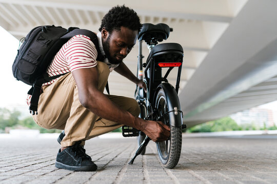 Black man fixing eco bike parked on pavement