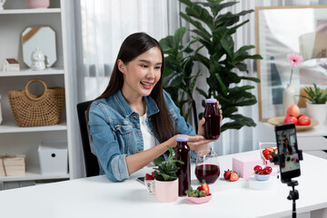 Smiling young beautiful Asian reviewing tasty mixed strawberry and cherry juice detox drinks,...