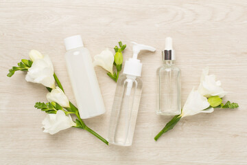 Facial cosmetic products with freesia flowers on wooden background, top view