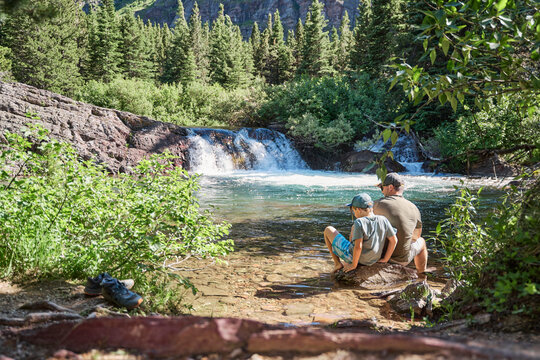 Father and son resting at the foot of a waterfall in Glacier