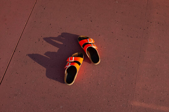 Orange sandals on a red wall with sunlight