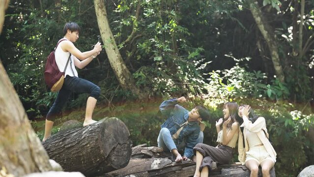 Young Asian man and woman enjoy outdoor lifestyle travel nature forest on summer holiday vacation. Happy generation z people friends using mobile phone taking picture together at waterfall lagoon.