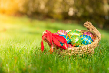 Easter eggs in basket in grass. Colorful decorated easter eggs in wicker basket. Traditional egg hunt for spring holidays. Morning magical light.	