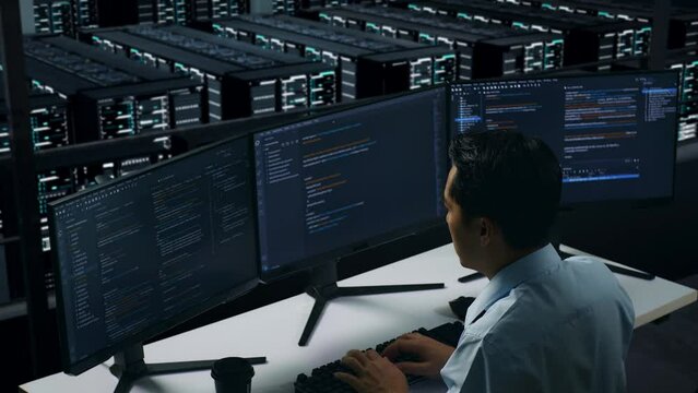 Side View Of Asian Man Developer Having Headache While Write Code With Multiple Computer Screens In Data Center