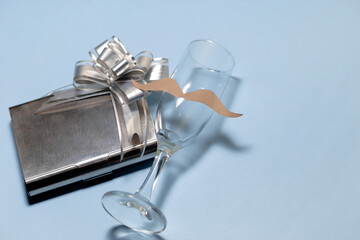 a glass cup with a mustache and on the side a gift in a gray and shiny box. Father's day. copyspace