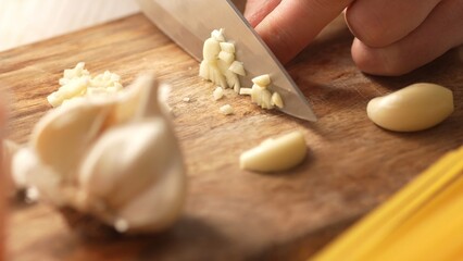 Chopping garlic on a cutting board. Fried Assassin's Spaghetti Cooking Step. Close-up, shallow dof.