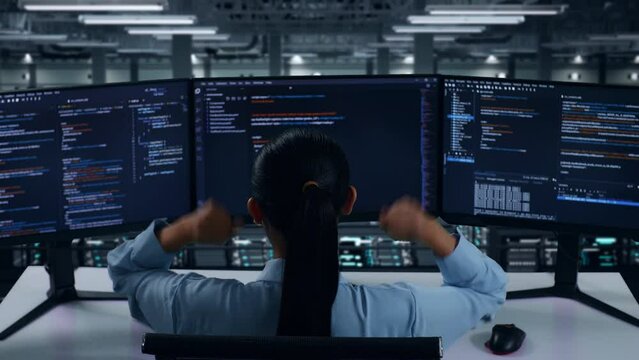 Back View Of Happy Asian Woman Developer Celebrating And Dancing While Write Code With Multiple Computer Screens In Data Center