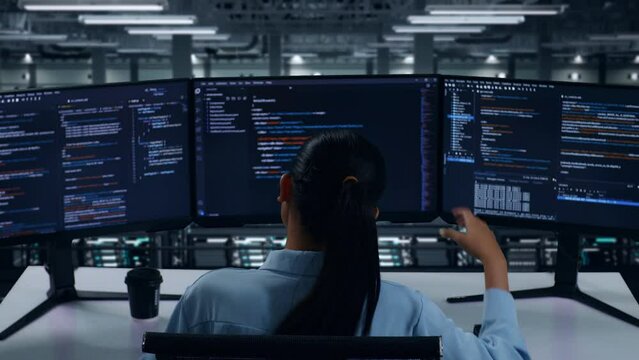 Back View Of Asian Woman Developer Having Headache While Write Code With Multiple Computer Screens In Data Center