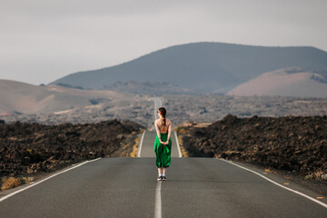 Woman in green dress in the middle of a long straight lonely road