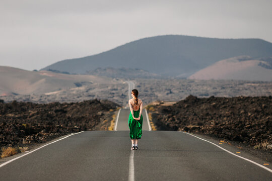 Woman in green dress in the middle of a long straight lonely road