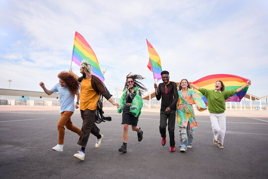 A group of LGBT people is leisurely walking down the street in the gay pride day parade holding colorful rainbow flags, enjoying a fun, friendship and happy event. Diverse men and women run together