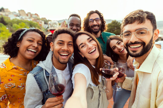 Happy young friends taking selfie group together enjoying summer party. Millennial people having fun toasting red wine at rooftop celebration