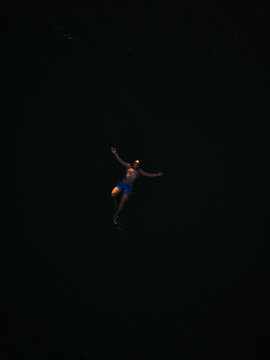 Young adult floating in dark water at sunset. 