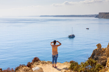 Fototapeta na wymiar Tourist woman standing on the edge of cliff, looking at the atlantic ocean and Algarve coastal. Ponta da Piedade, Lagos, Algarve, Portugal