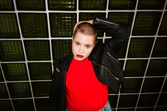 Young female with shaved head at green wall