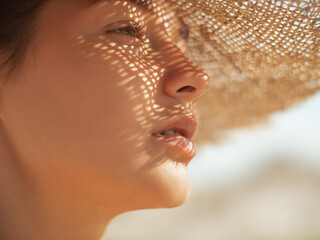 Beach sun hat woman during vacation. Close-up of a girl's face in straw sunhat enjoying the sun...