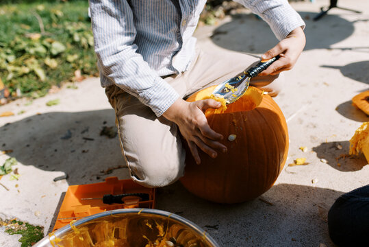 toddler boy making jack o lantern and is carving a pumpkin