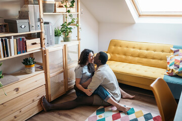 Diverse pregnant couple kissing at home