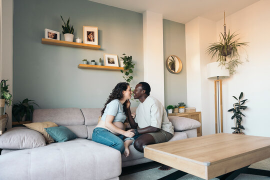 Diverse pregnant couple kissing at home