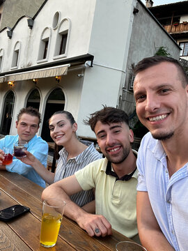 Group of friends taking selfie and toasting with cocktails at bar