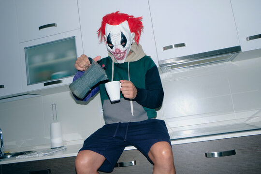 man wearing a clown mask in the kitchen pouring some coffee