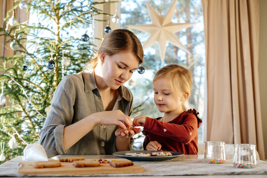 Female with kid decorating gingerbread cookie with sprinkles