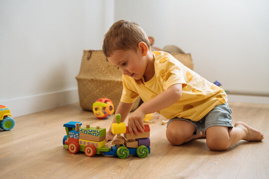 Cute kid playing with toy train on floor in daylight