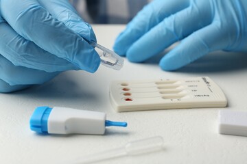 Doctor dropping buffer solution onto disposable multi-infection express test cassette at white...
