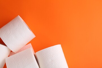 Soft toilet paper rolls on orange background, flat lay. Space for text