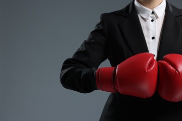 Businesswoman in suit wearing boxing gloves on grey background, closeup. Space for text